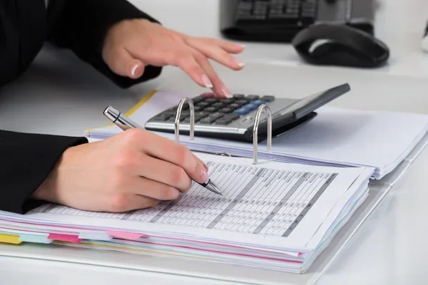 primer plano de manos realizando un control presupuestario en un escritorio, con calculadora y tomando notas