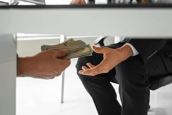 primer plano de manos recibiendo dinero por debajo de la mesa, representando un soborno y la falta de ética empresarial
