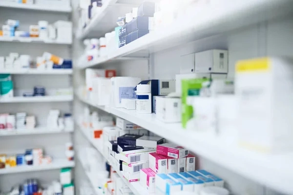Primer plano de estanterías blancas en una farmacia, llenas de diversas cajas y envases de medicamentos organizados. La imagen tiene un enfoque selectivo que resalta los productos en primer plano sobre un fondo ligeramente desenfocado