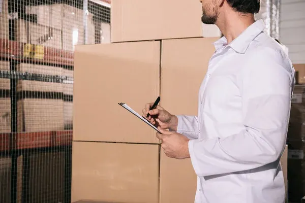 hombre en camisa realizando el control de stock frente a cajas en un almacén