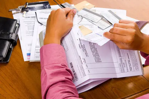 Persona rompiendo facturas y documentos financieros sobre una mesa con tarjetas de crédito, representando la liquidación de deudas o el cierre contable de un negocio bajo el régimen NRUS