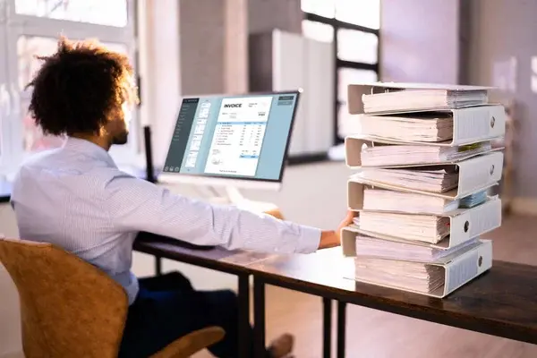Persona en una oficina realizando la transición de archivos físicos a libros electrónicos SUNAT mediante un software de facturación en su monitor.